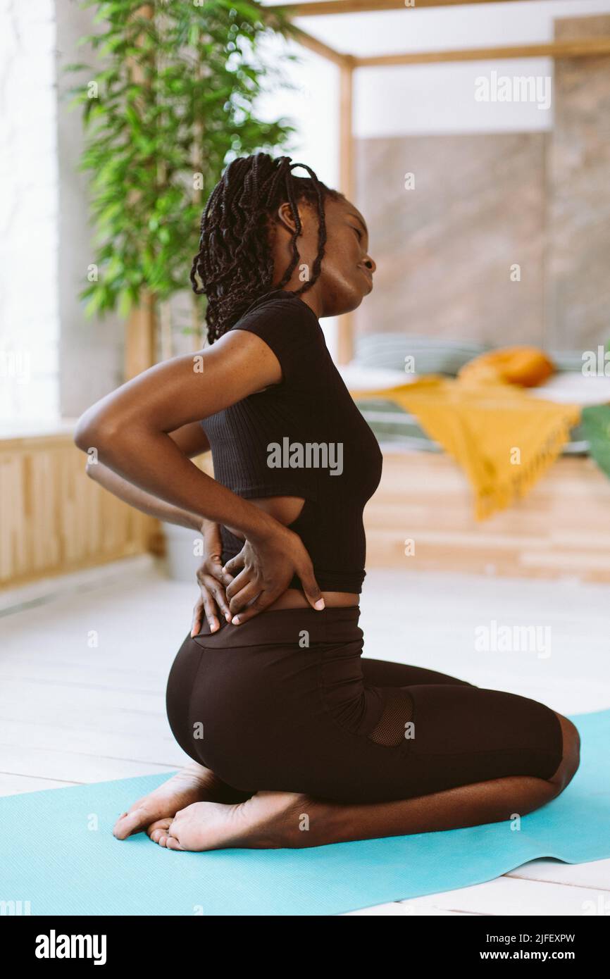 Vertical African American multicultural sportswoman with dreadlocks stretching, inclining, do yoga. Backache, healthcare Stock Photo