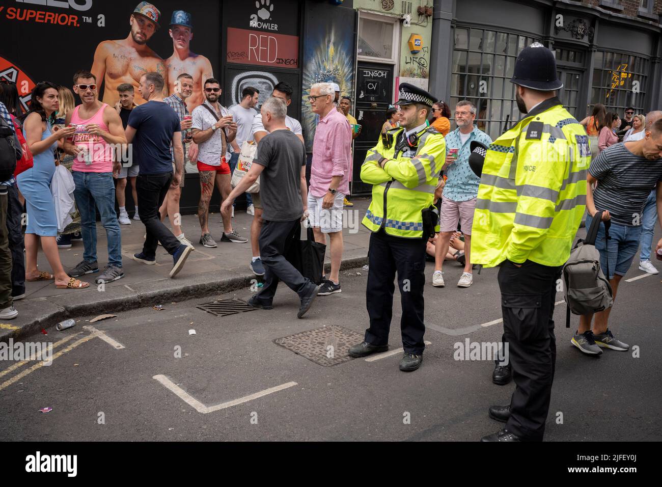 Wearing uniforms, Met police officers watch members of the LGBTQ+ community gather in Soho streets during the 50th Gay Pride celebrations, on 2nd July 2022, in London, England. Stock Photo