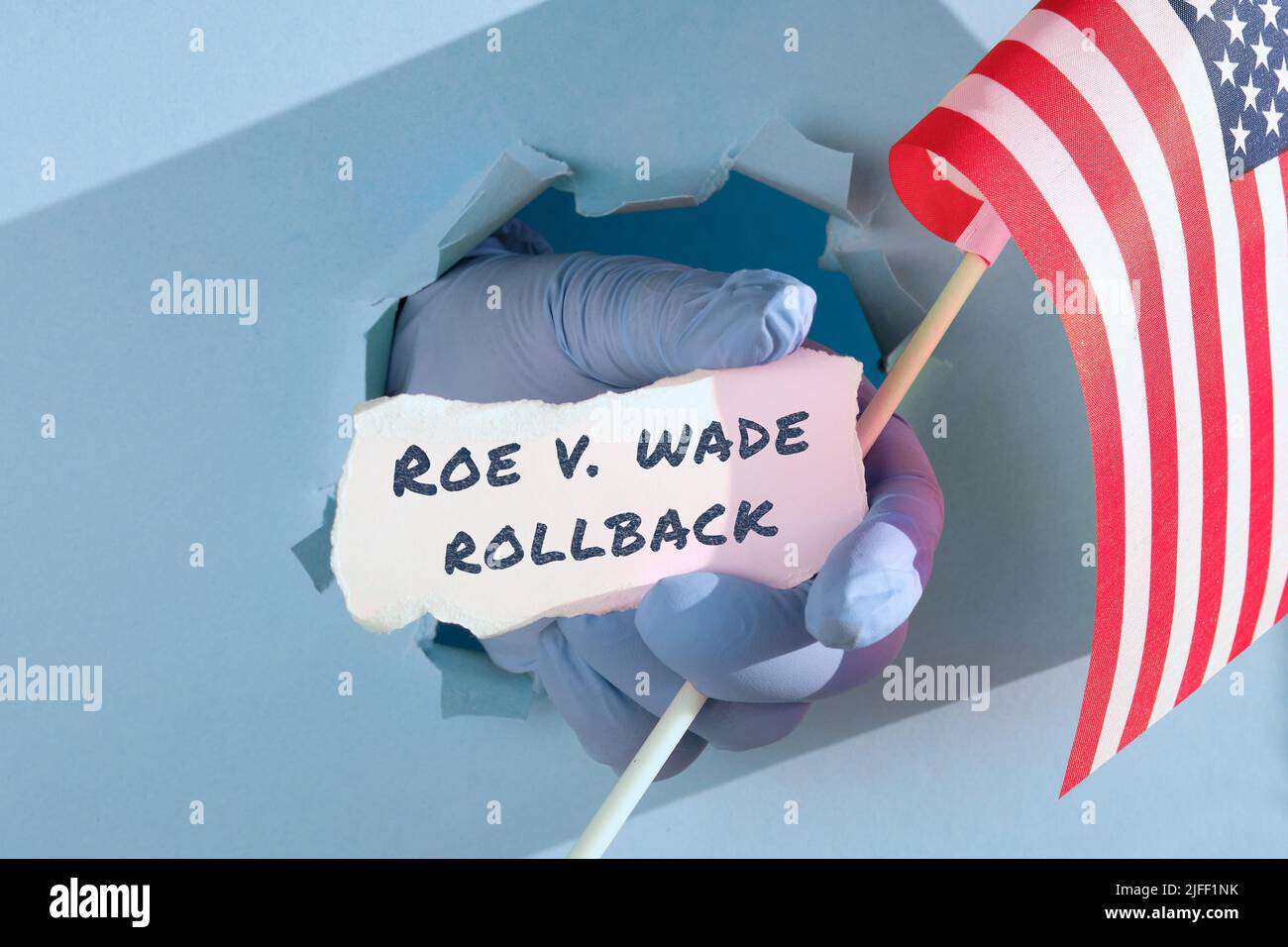 Text Roe vs Wade Rollback on scrap of paper. Medics, doctors hand in glove holding USA american flag and scrap of paper Stock Photo