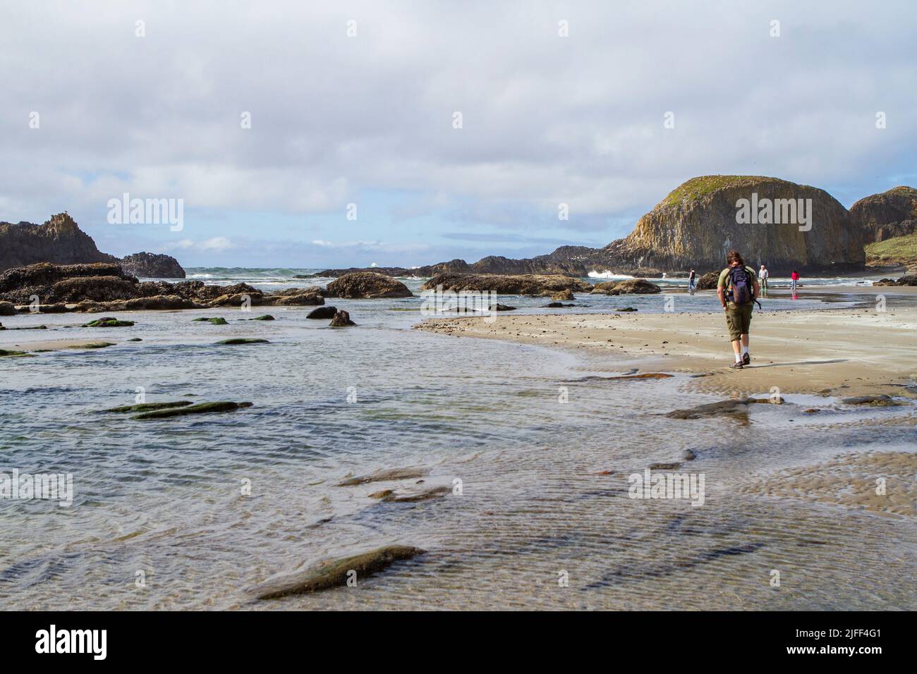 Several tourists, including a man with a daypack, walk along the beach at Seal Rock State Recreation Site on the central coast of Oregon, USA. Stock Photo