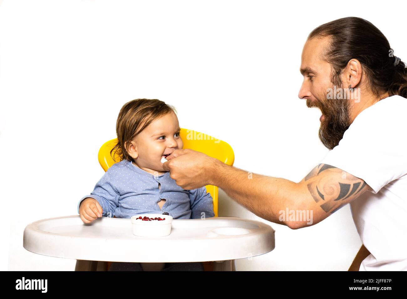 Dad laughs and feeds the baby on on the highchair. The concept of spending time with children.Front view photo on a light background. Life style Stock Photo