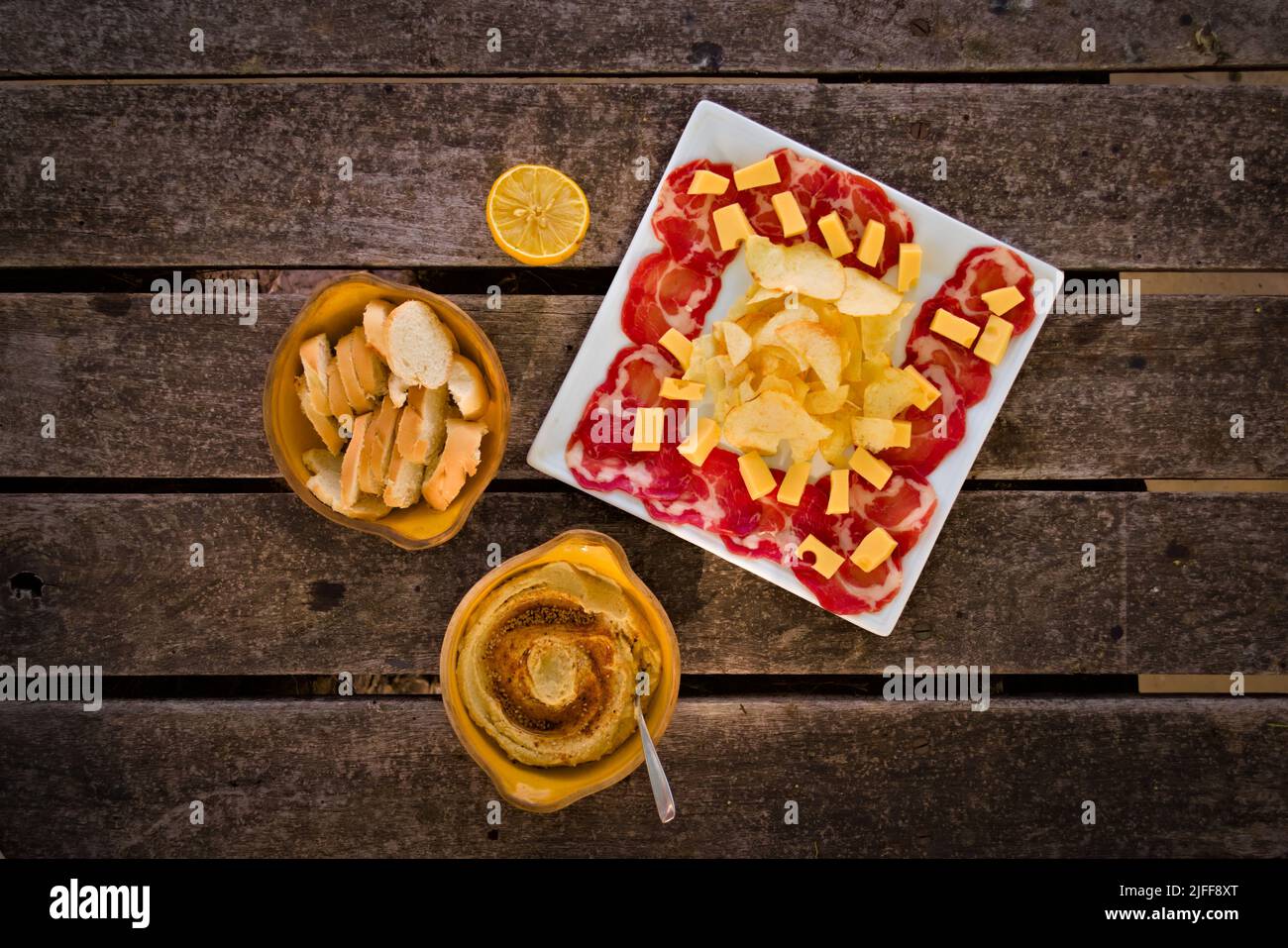 Cured ham, cheese, bread and hummus. Traditional mediterranean appetizer. Top down view. Stock Photo