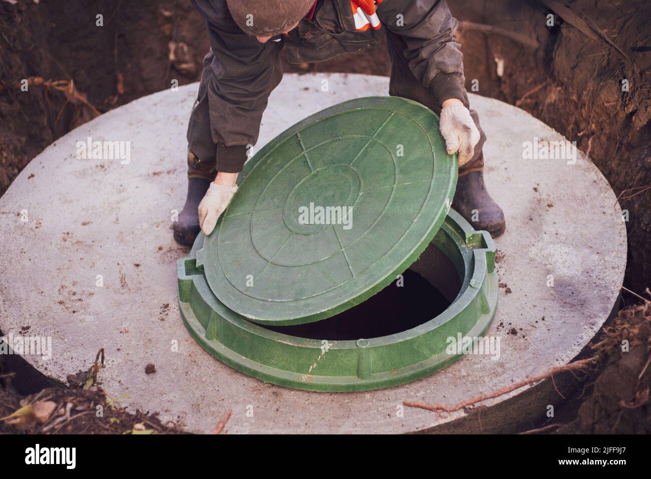 A worker lifts the manhole cover of a sewer well. Construction and ...