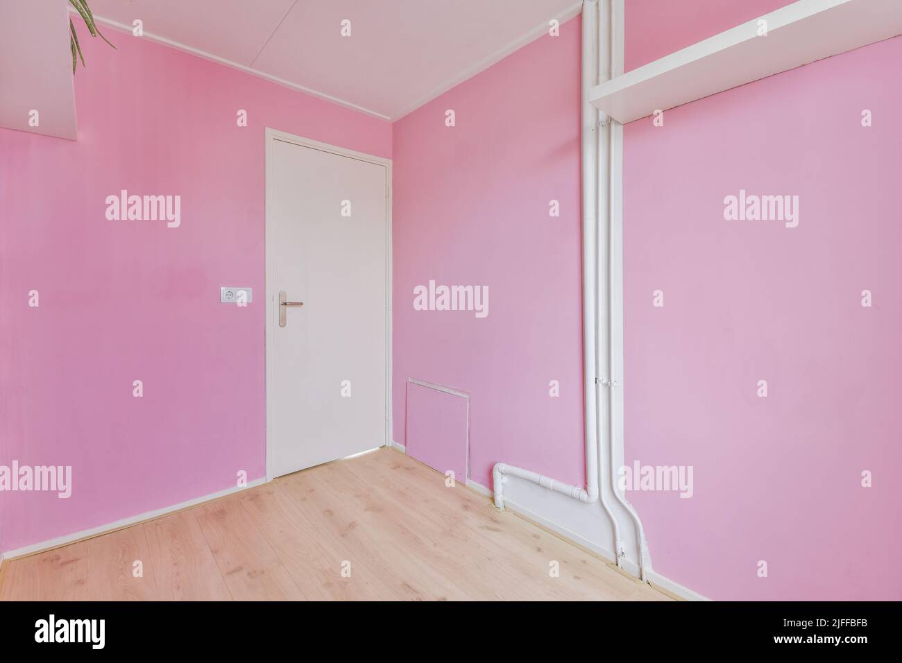 Spacious empty room with pink walls and white pipes, shelf and door