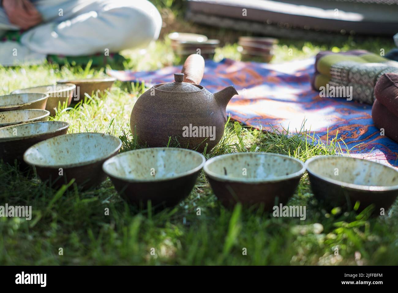 Tea ceremony setting in nature during summer. Handicraft ceramic tea bowls and clay pot. Outdoor tea circle. Calm and relaxing meditation tradition. Stock Photo