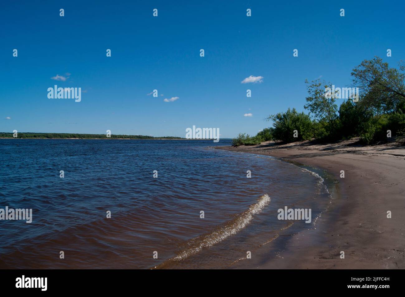 Deep cold ryokana in the north of Russia. The seasons are summer. A sandy beach with green bushes growing on it. White clouds in the blue sky - Stock Image