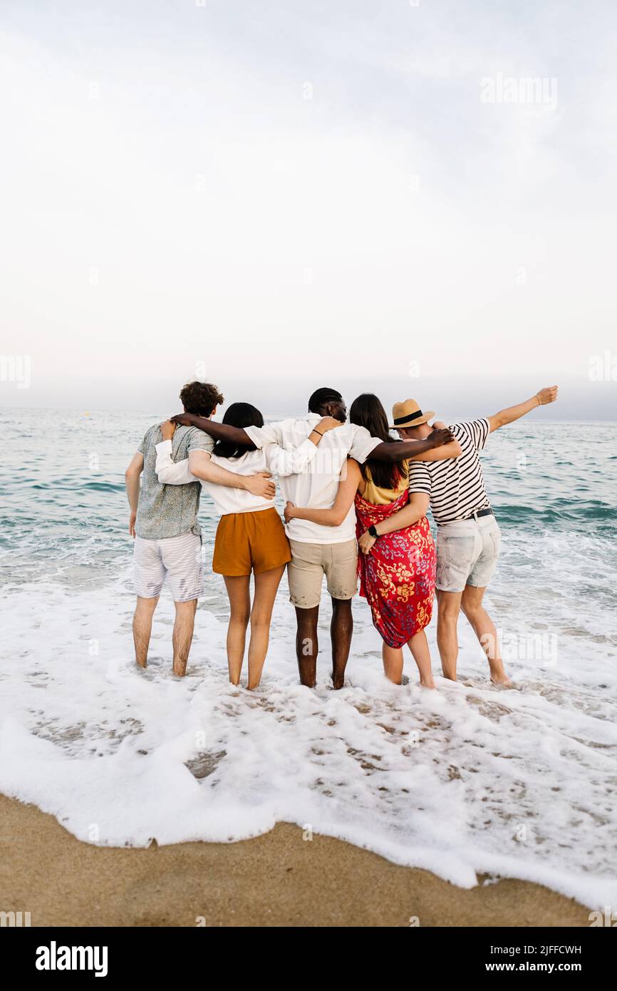 Group of young people hugging each other and enjoying sunset at beach Stock Photo