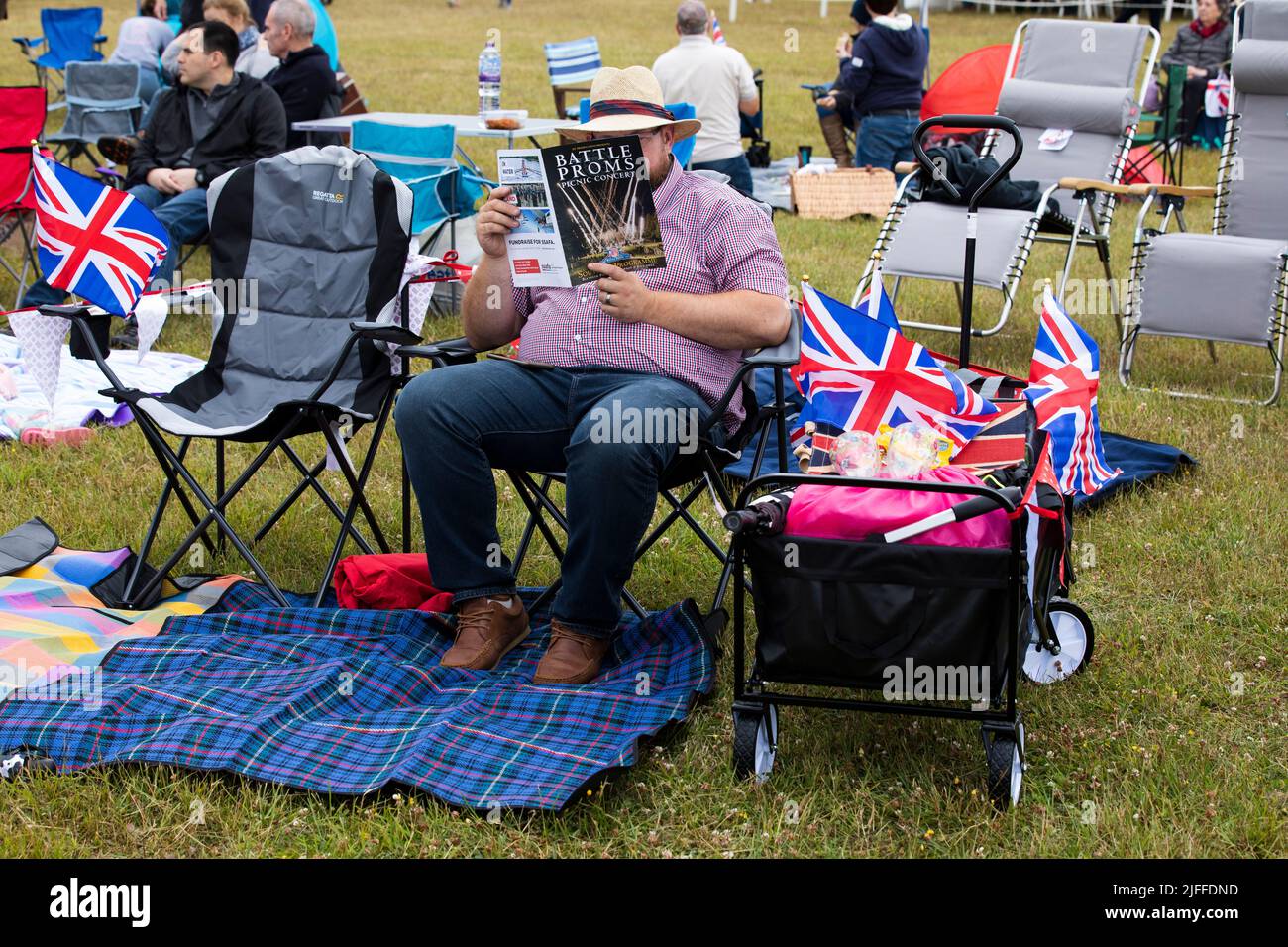 Woodstock, Oxfordshire, UK. 2nd July 2022. Man seated reading programme for Battle Proms with trolly and Untion Jacks. Battle Prom Picnic Concerts. Blenheim Palace. United Kingdom. Credit: Alexander Caminada/Alamy Live News Stock Photo