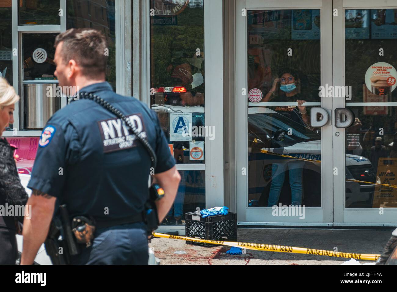 July 2, 2022: Dunkin' Donuts staff look out the store window after a man was shot in front of it in Manhattan's Lower East Side, New York Stock Photo