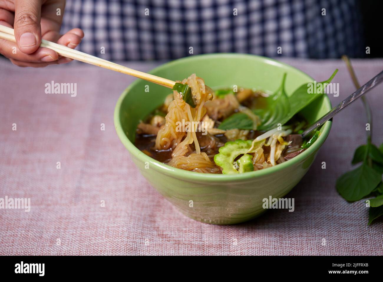 woman hand uses chopsticks to pickup rice stick noodles on table Stock Photo