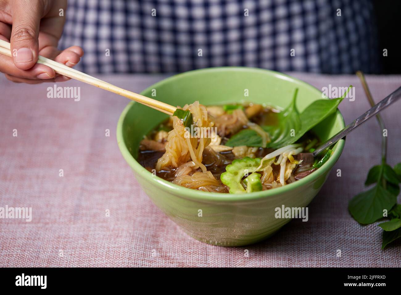 woman hand uses chopsticks to pickup rice stick noodles on table Stock Photo