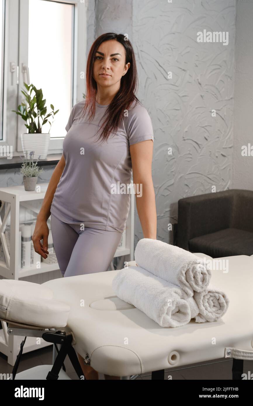Female massage specialist, physiotherapy expert or massage specialist in professional aesthetic medicine salon waiting for client by couch. Modern Stock Photo