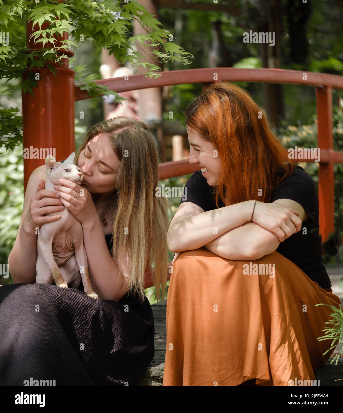 Happy ginger hair woman with friend in well-groomed park or garden. Support and healthy way of life. Female with cat in her 40s having rest outdoors Stock Photo