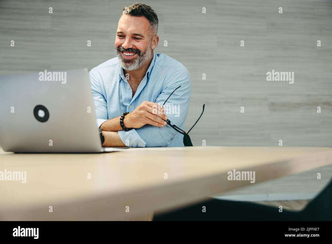 Happy mature businessman attending an online meeting with his business associates. Cheerful entrepreneur having a video conference while working remot Stock Photo
