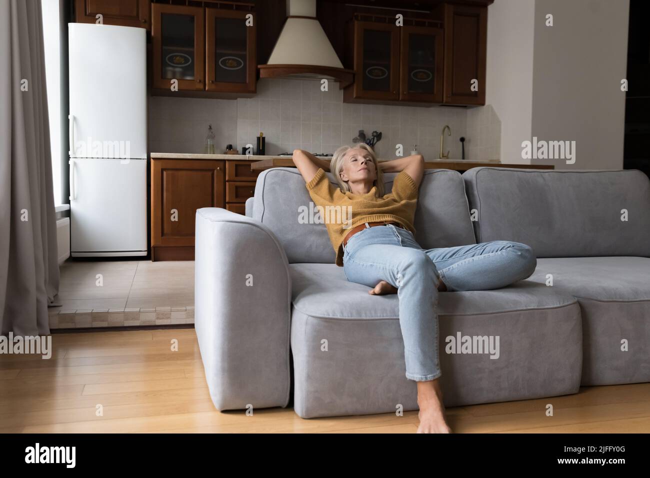 Peaceful older woman leaned on sofa relaxing at home Stock Photo