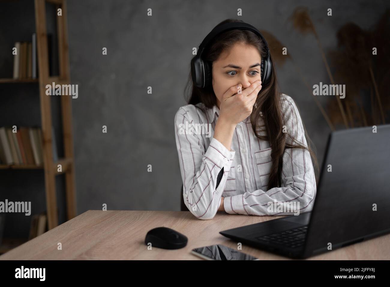 Young female watching scary movie, hiding face in fear, online film service. Hispanic young woman in headphones watching drama movie, worrying for Stock Photo