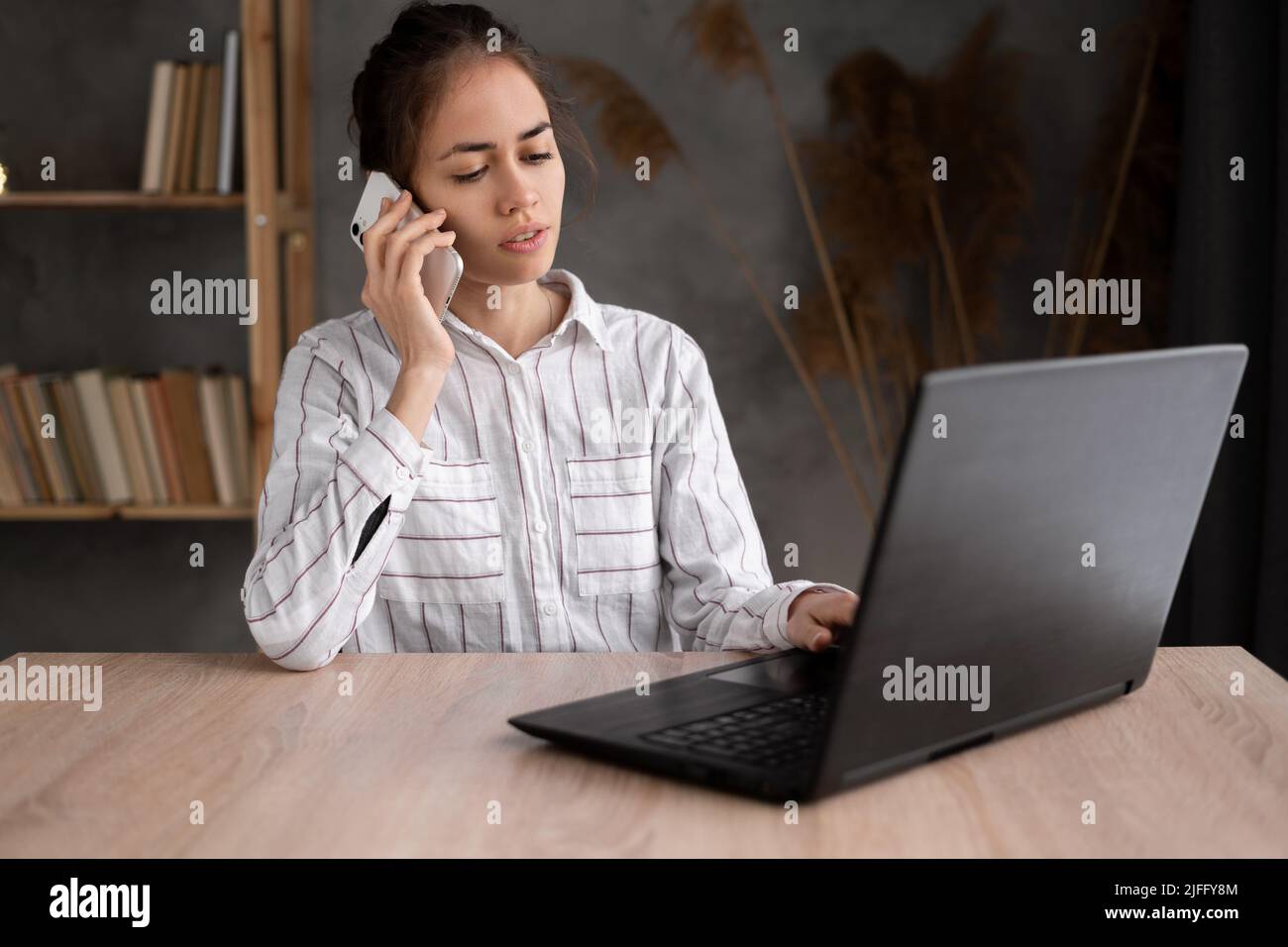 Single happy female business owner call on phone and working on laptop computer at desk. Stock Photo
