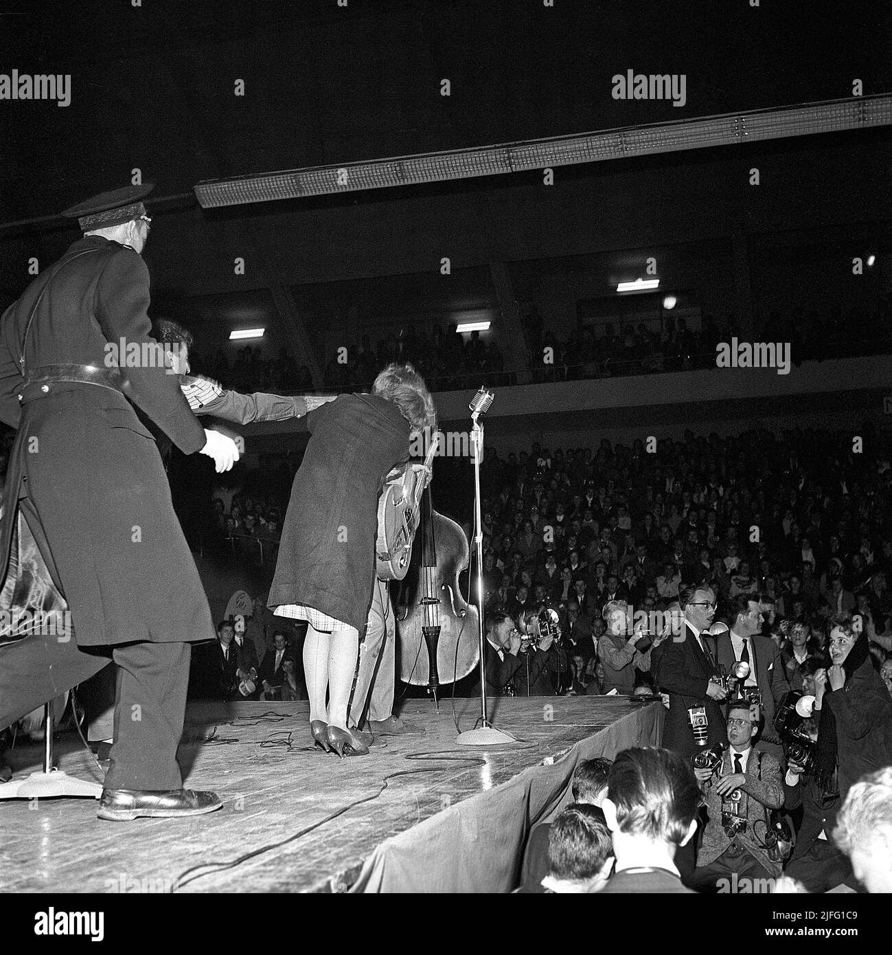 Tommy Steele. English entertainer regarded as Britain's first teen idol and rock and roll star. Born december 17 1936. Picture taken when he performed in Stockholm Sweden April 19 1958. A woman from the audience has taken a chance to run up on stage to give her idol a hug, and is soon being taken off the stage by a policeman. Stock Photo