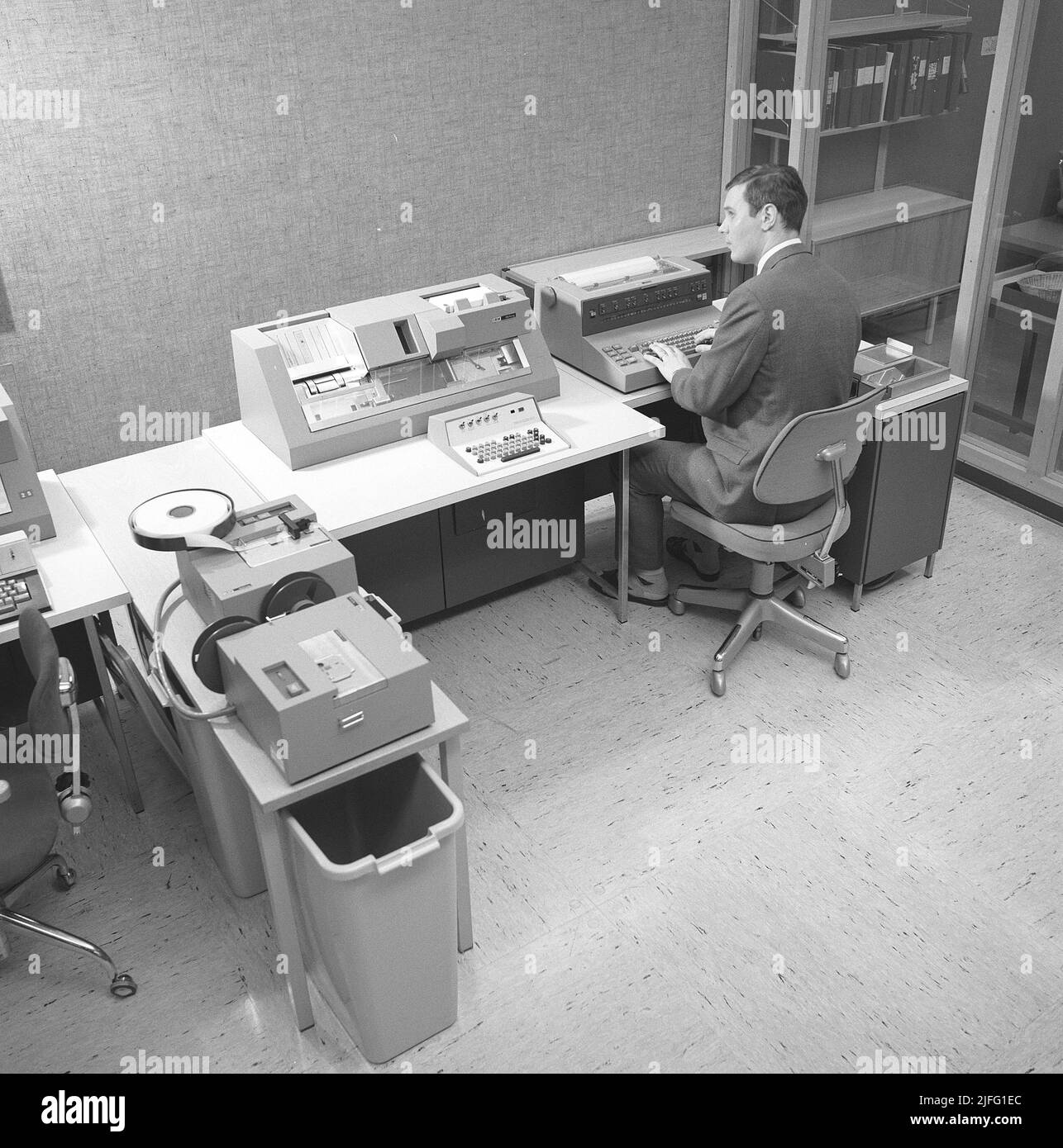 Data handling the 1960s. Interior of a room with IBM computer equipment for reading and entering information into the mainframe computer. A man at a keyboard controls the software, handling, register and reading information. The equipment are parts of an IBM system 360. It was frequently seen in the american television-series Mad Men.  Picture taken 1965 Kristoffersson ref DY127-5 Stock Photo