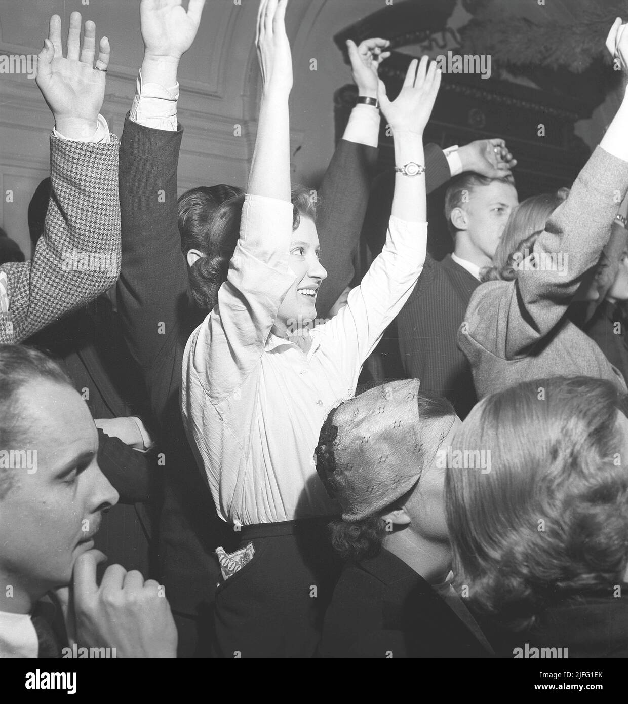 Fun in the 1950s. An audience of young women and men are visible exited, shouting, laughing at something on stage. They rise their hands and cheer. Sweden 1952 Kristoffersson ref BF7-4 Stock Photo
