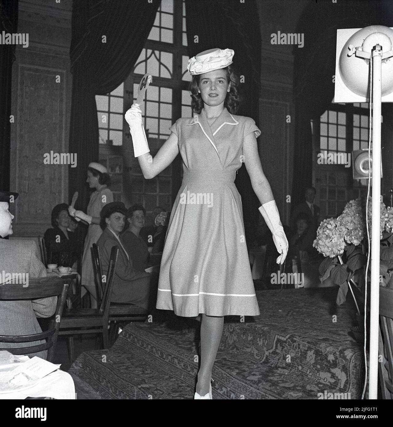 Women's fashion in the 1940s. A young woman in a 1946 outfit. A dress with the right length, matching hat and gloves. The fashion show of ladies fashion of this year goes on in front of people in an audience. Sweden 1946  Kristoffersson T148-5 Stock Photo