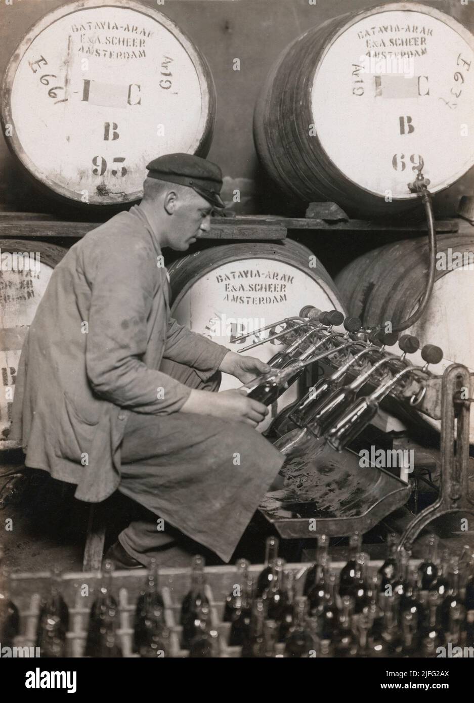Wine history at the turn of the 19th-20th century. Picture shows a man working at the wine merchant company J. Cederlunds Söner in Sweden, tapping Punsch from the barrels into bottles. The alcoholic beverage Punsch refers to a specific type of alcoholic liqueur and punch popular in Sweden. It is most frequently described as Swedish Punsch. Is is made by the mixing of spirits arrack, brandy or rum with arrak tea, sugar and water and was first brought to Sweden from Java in 1733. Punsch usually has 25% alcohol by volume. It is drunk both warmed and chilled. Some believe the word punch/punsch cam Stock Photo