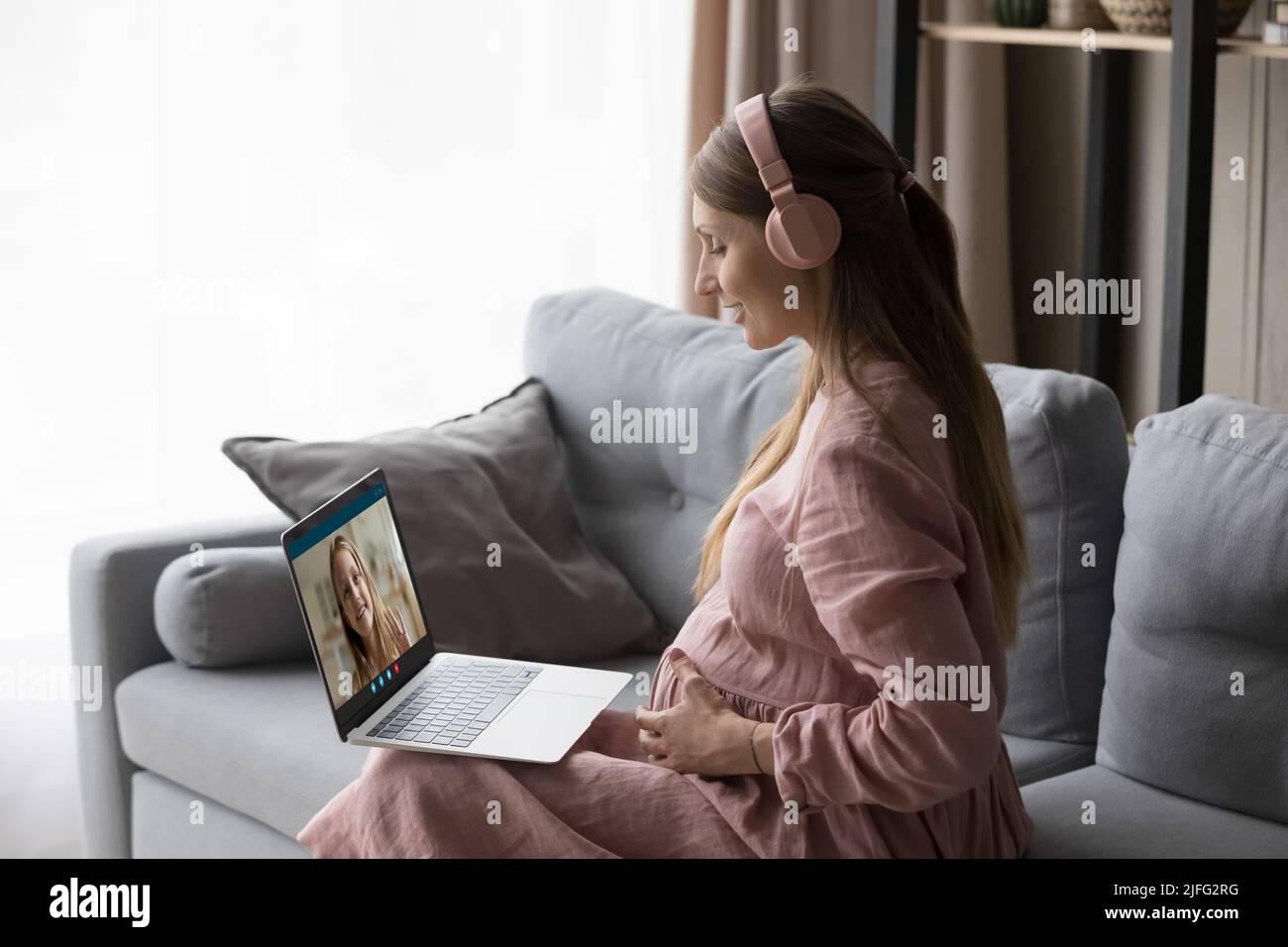 Pregnant woman use laptop makes videocall communicates to little daughter Stock Photo