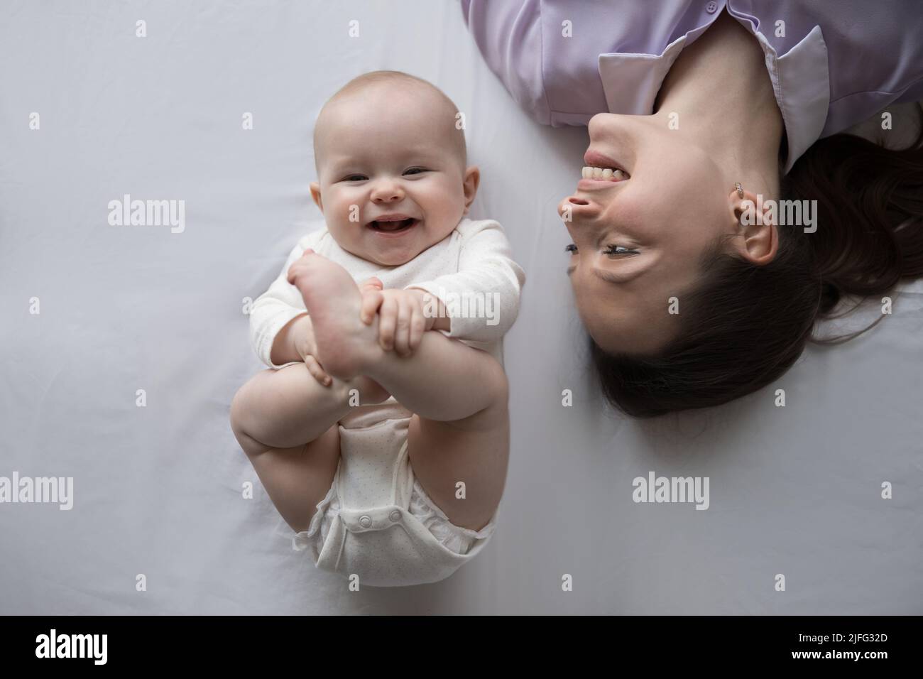 Lovely baby lying on bed near mother, above closeup shot Stock Photo