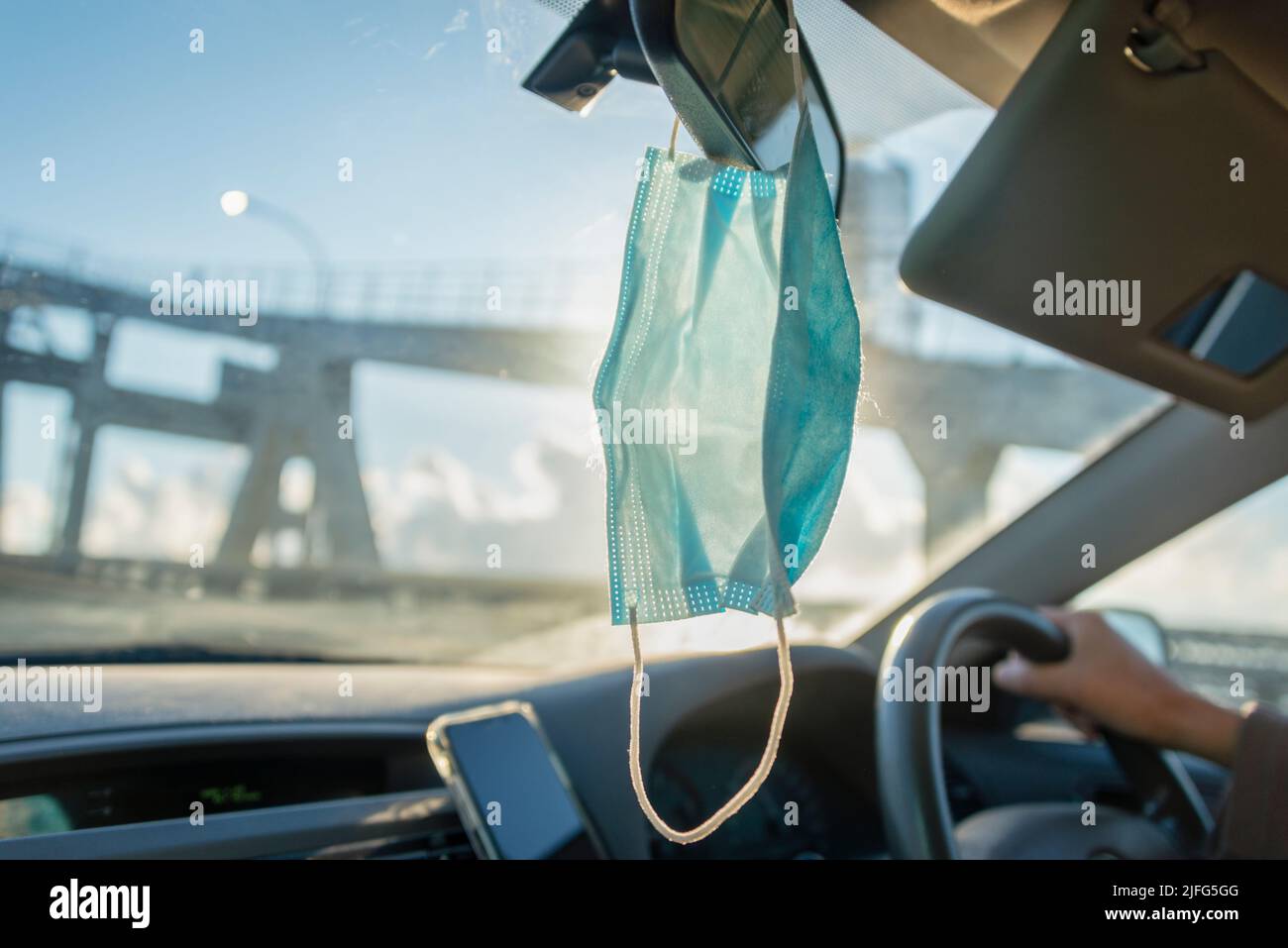 Facemask hanging on the car mirror inside a car, driving on Auckland Harbour Bridge. Stock Photo