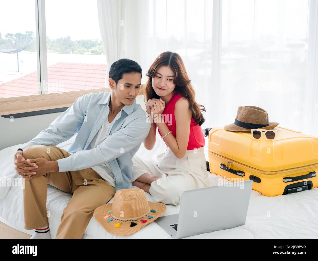 The girlfriend is begging and persuading her boyfriend to take a summer trip. Young cute Asian woman and handsome man looking at the laptop display on Stock Photo