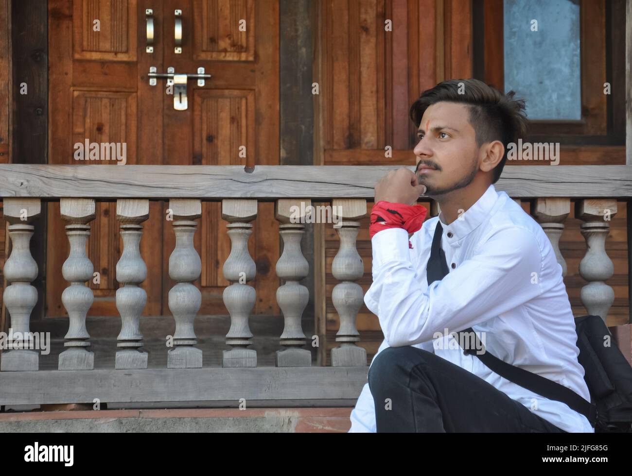 Side view of a young guy looking ahead while sitting on temple stairs posing with hand on chin Stock Photo