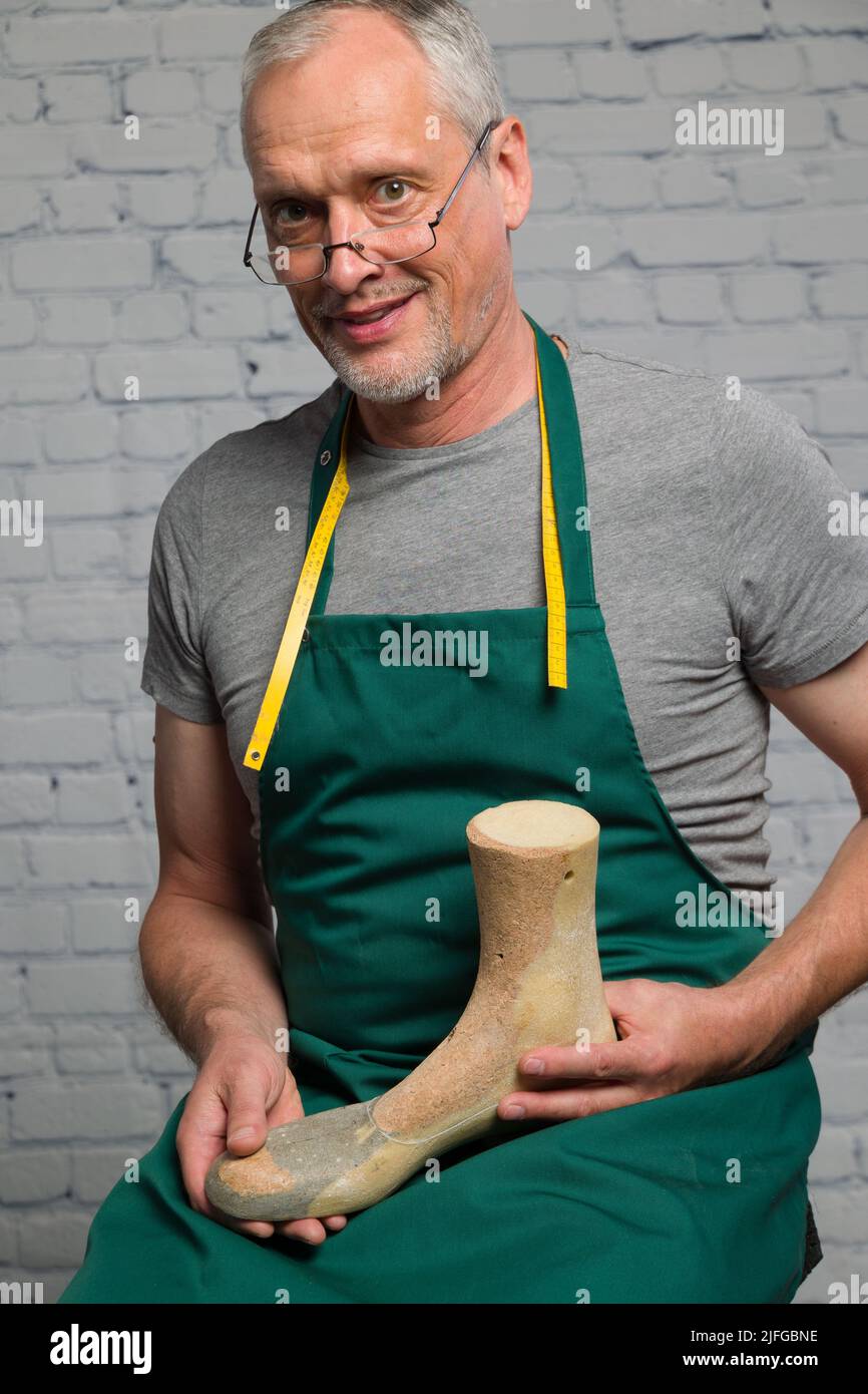 an elderly shoemaker wearing a green apron is presenting an individual made wooden last to make an individual orthopedic shoe Stock Photo