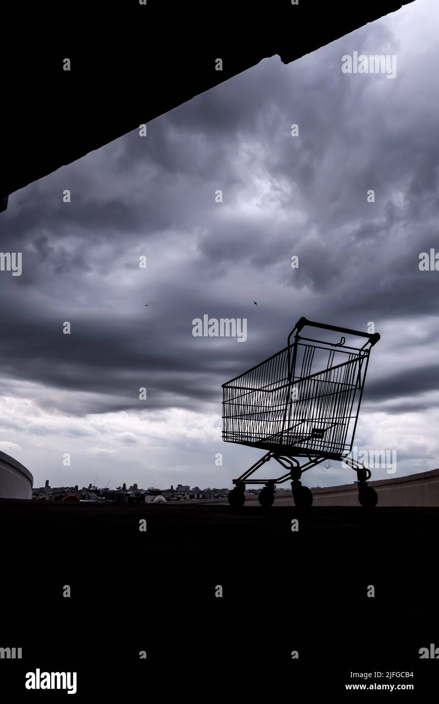 A shopping cart on a rooftop car park of an abandoned mall during the Coronavirus outbreak, dark rain clouds in the background. Stock Photo