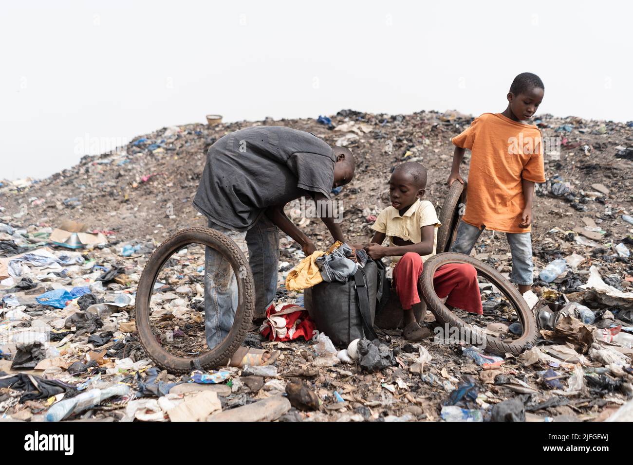 Three homeless street boys in a landfill with their daily loot of garbage to recycle and sell; condition of slum children in Africa Stock Photo