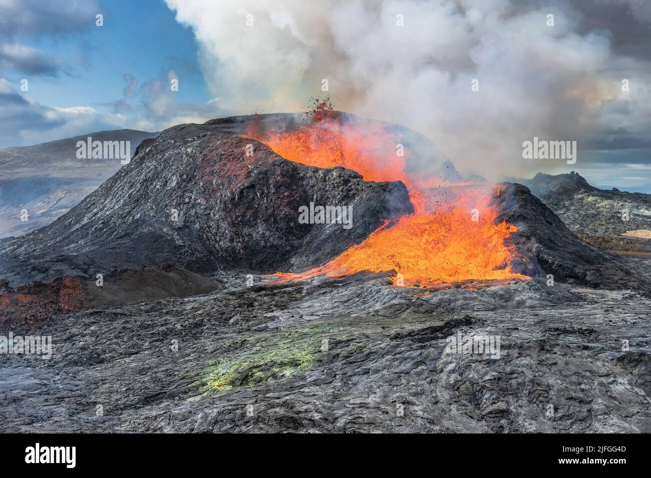 Lava fountains from the volcanic crater in Iceland. Landscape on Reykjanes peninsula in spring with sunshine. Liquid lava flows out of the side Stock Photo