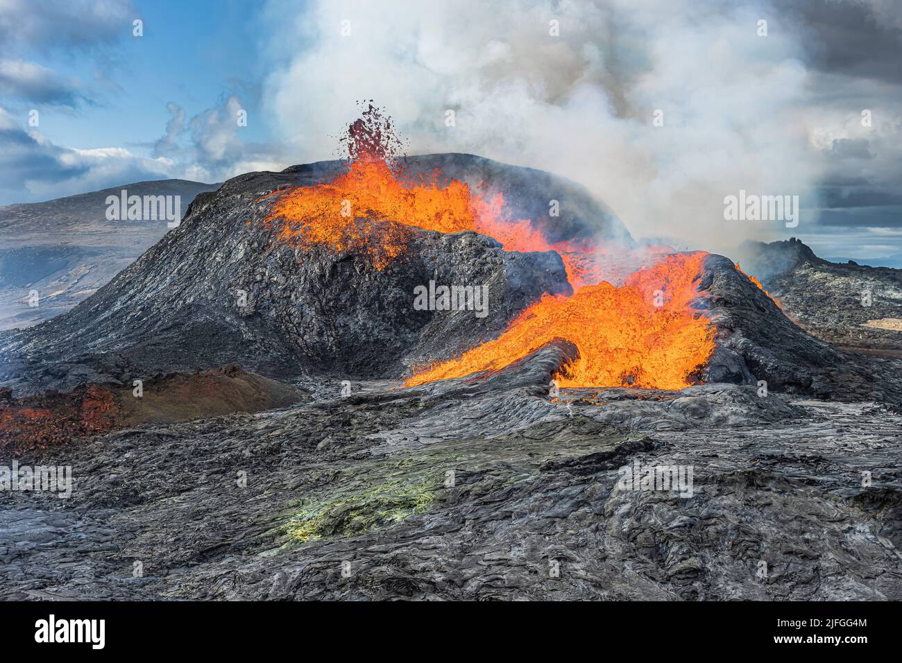 Active volcano on Iceland's Reykjanes Peninsula. Small lava fountain from the crater. Landscape in spring with sunshine. Liquid lava flows out of the Stock Photo