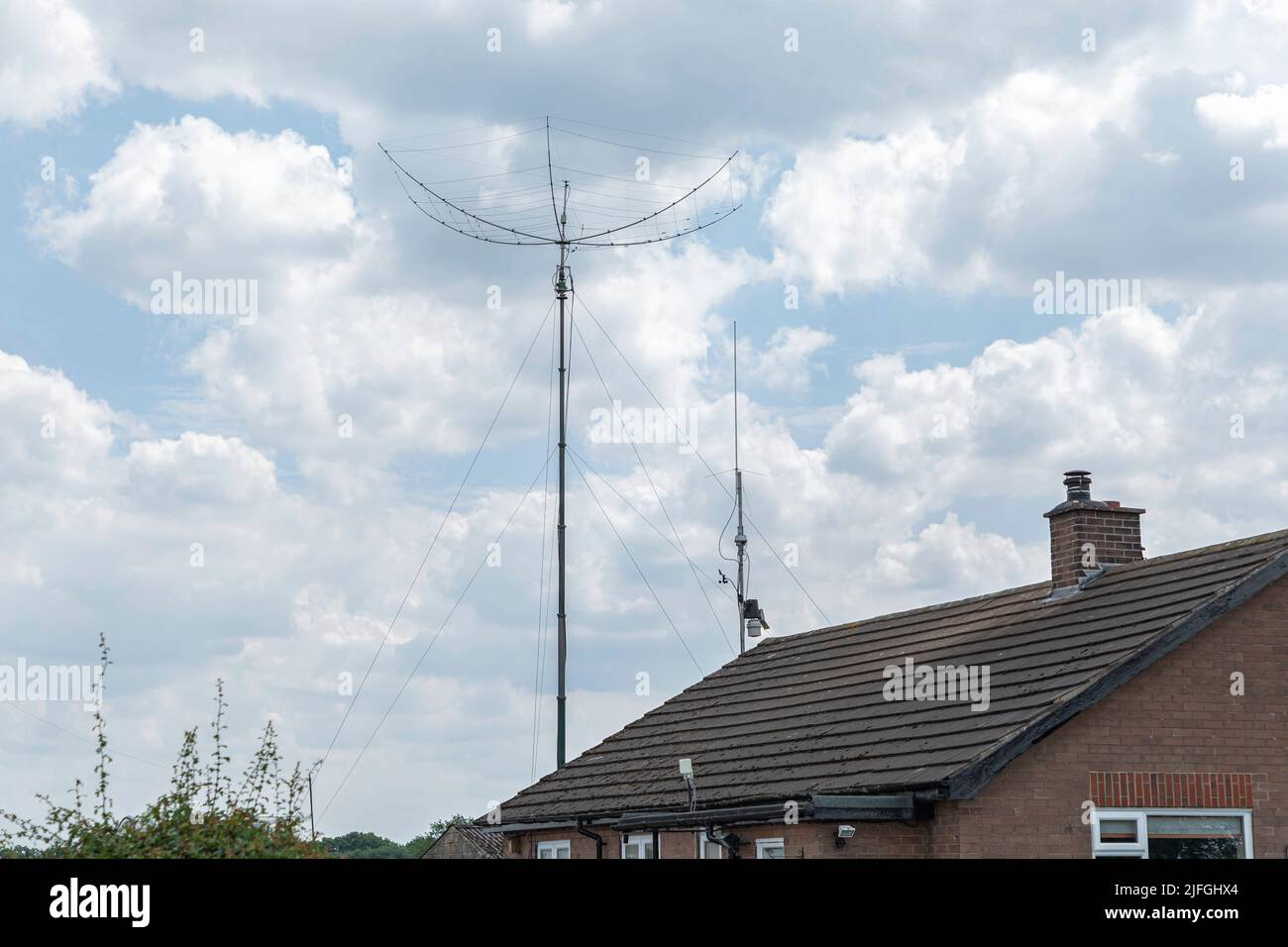 Small bungalow with radio AM umbrella shaped arial against a blue sky with clouds Stock Photo