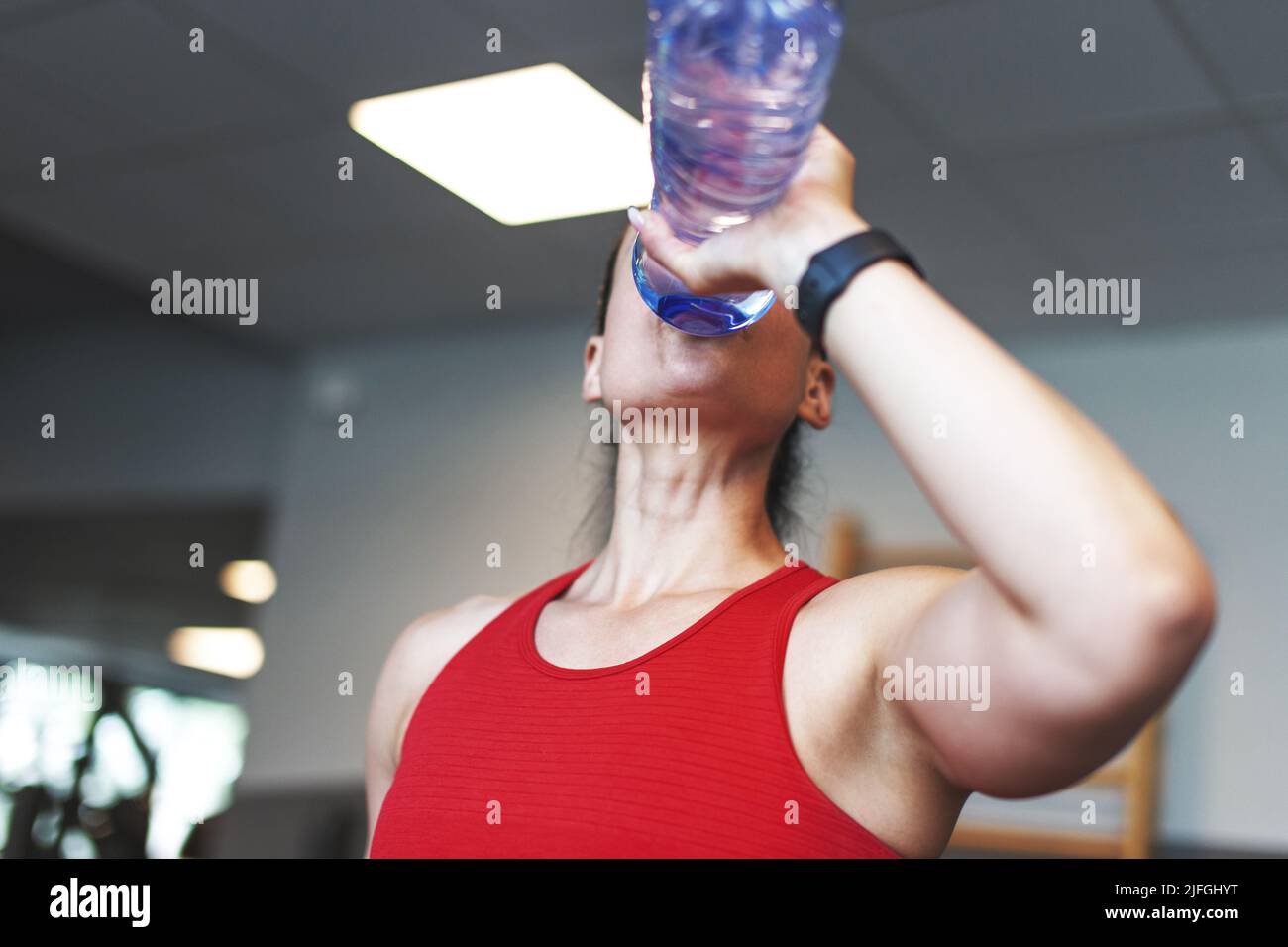 Young Caucasian woman drinking water from bottle in gym Stock Photo