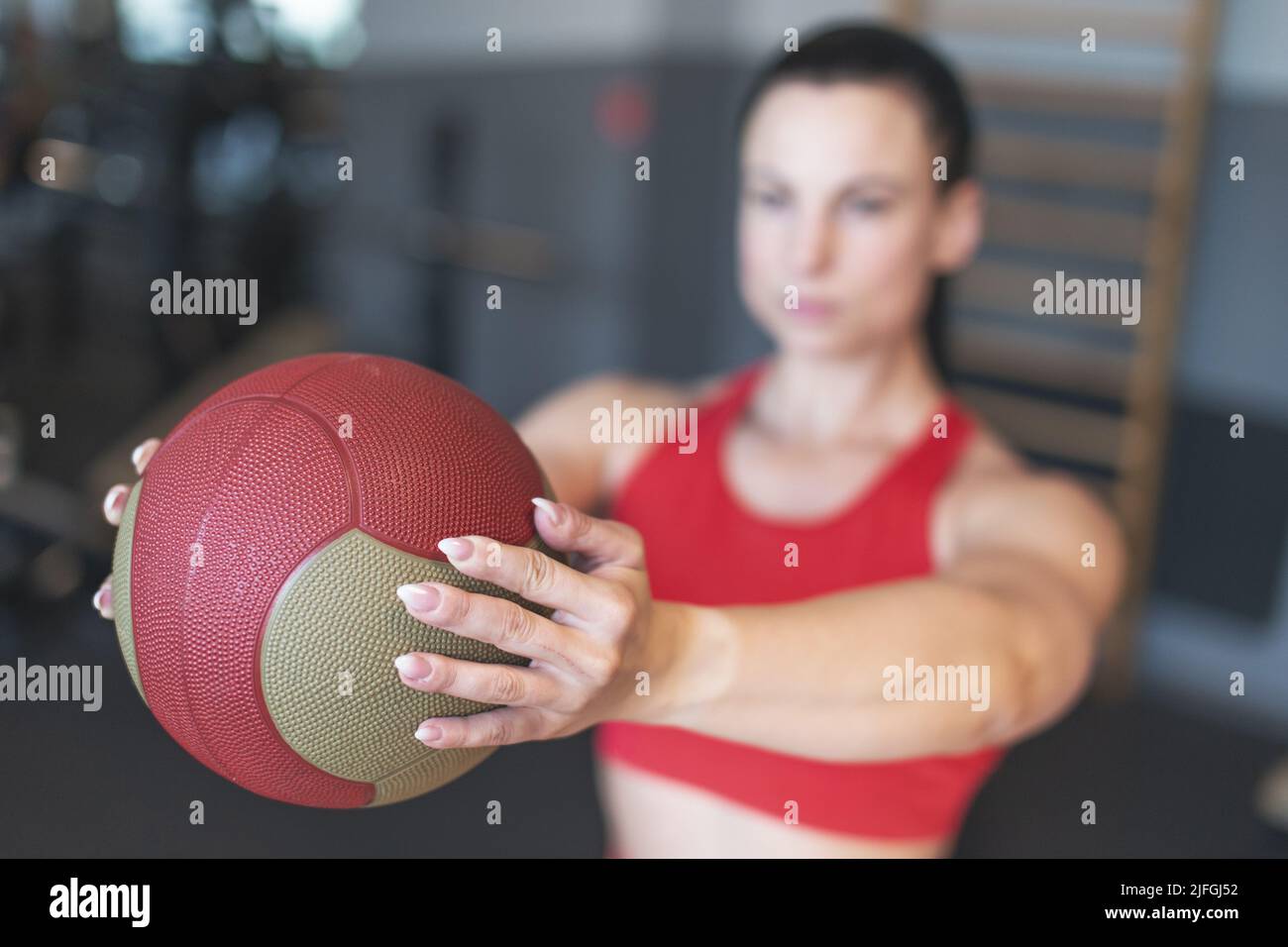Young Caucasian woman holding medicine ball in gym, depth of field Stock Photo