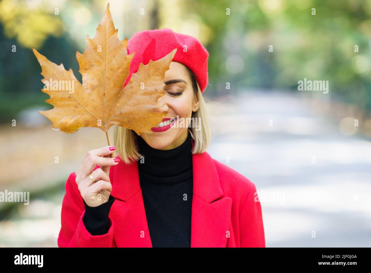 Smiling woman covering face with dry leaf Stock Photo