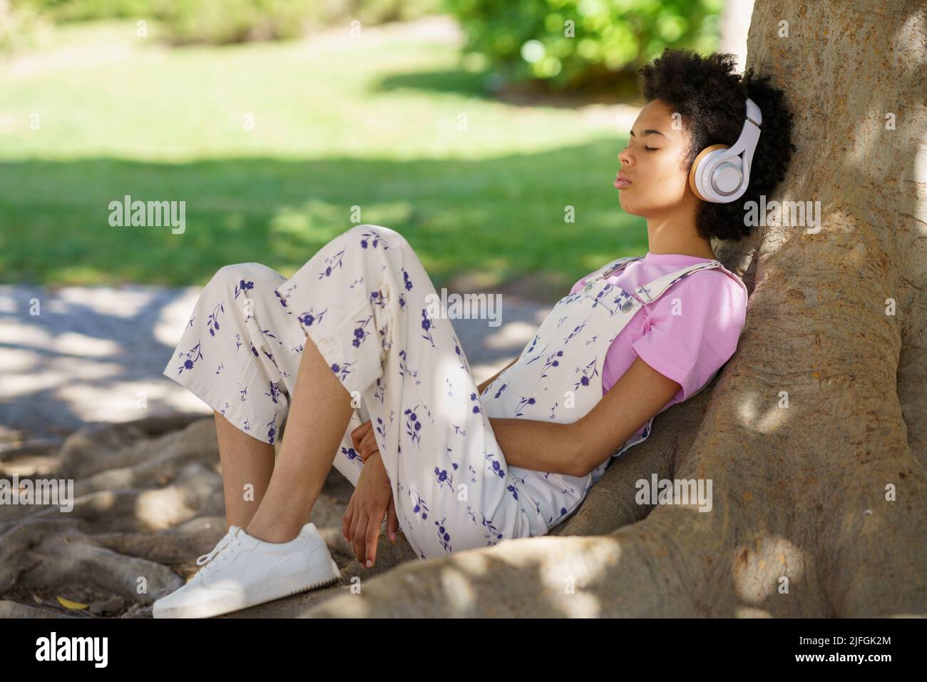 Black woman listening to music near tree Stock Photo