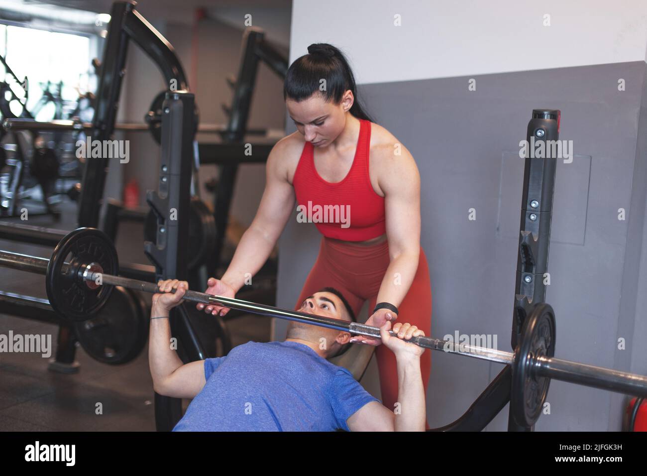 Young personal trainer helps to client doing bench press Stock Photo