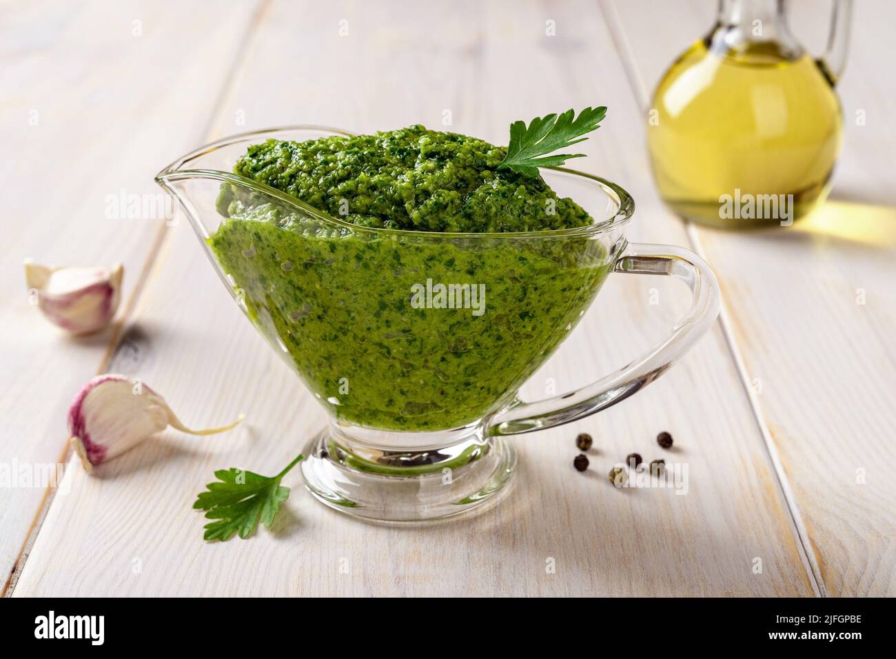 Green sauce in a gravy boat on a table. Chimichurri dipping sauce from fresh parsley, garlic cloves, olive oil and lemon juice. Salsa verde. Front vie Stock Photo