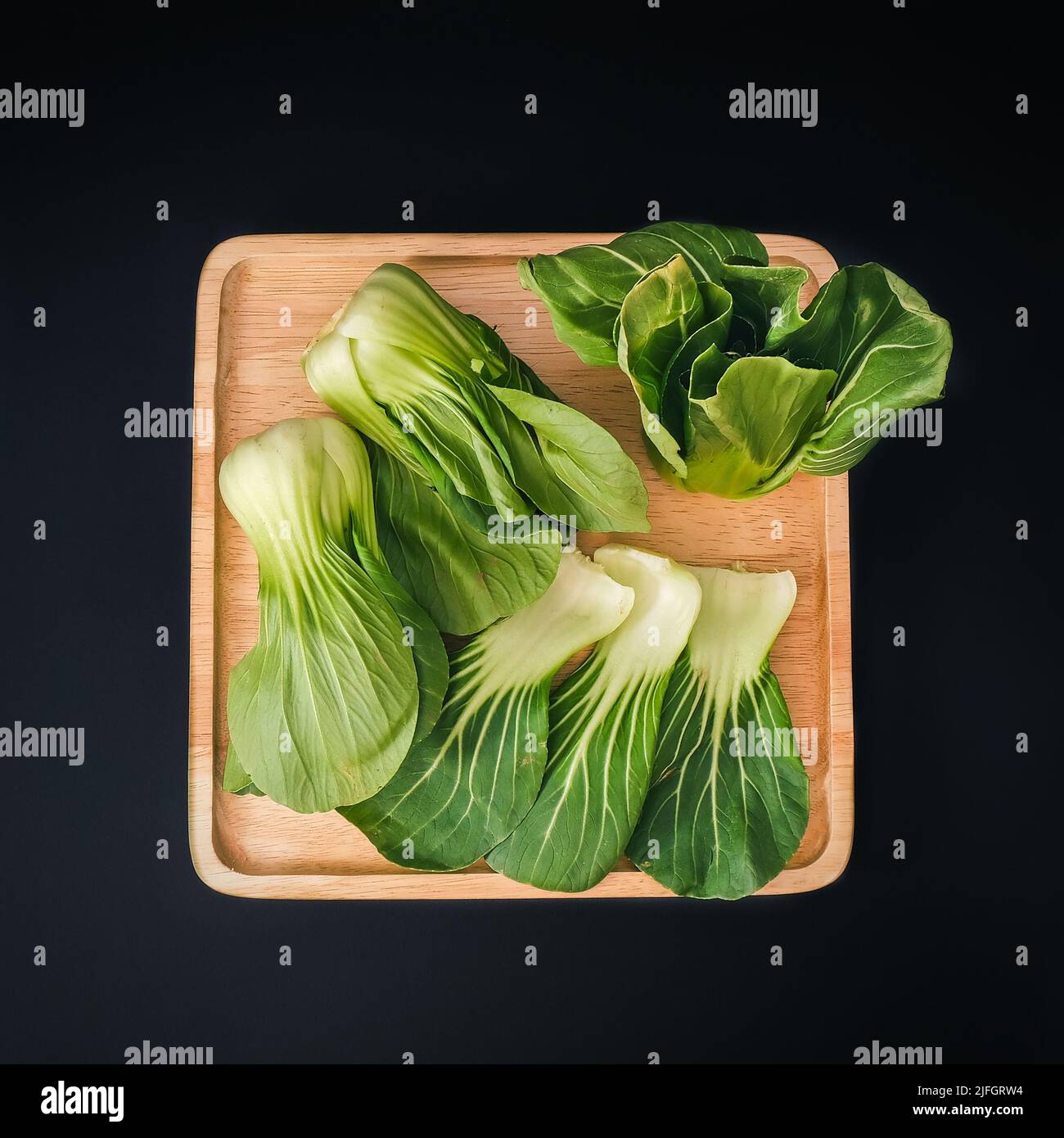 Organic green Baby Bok Choy or Brassica rapa chinensis on wooden plate on black background.  Stock Photo