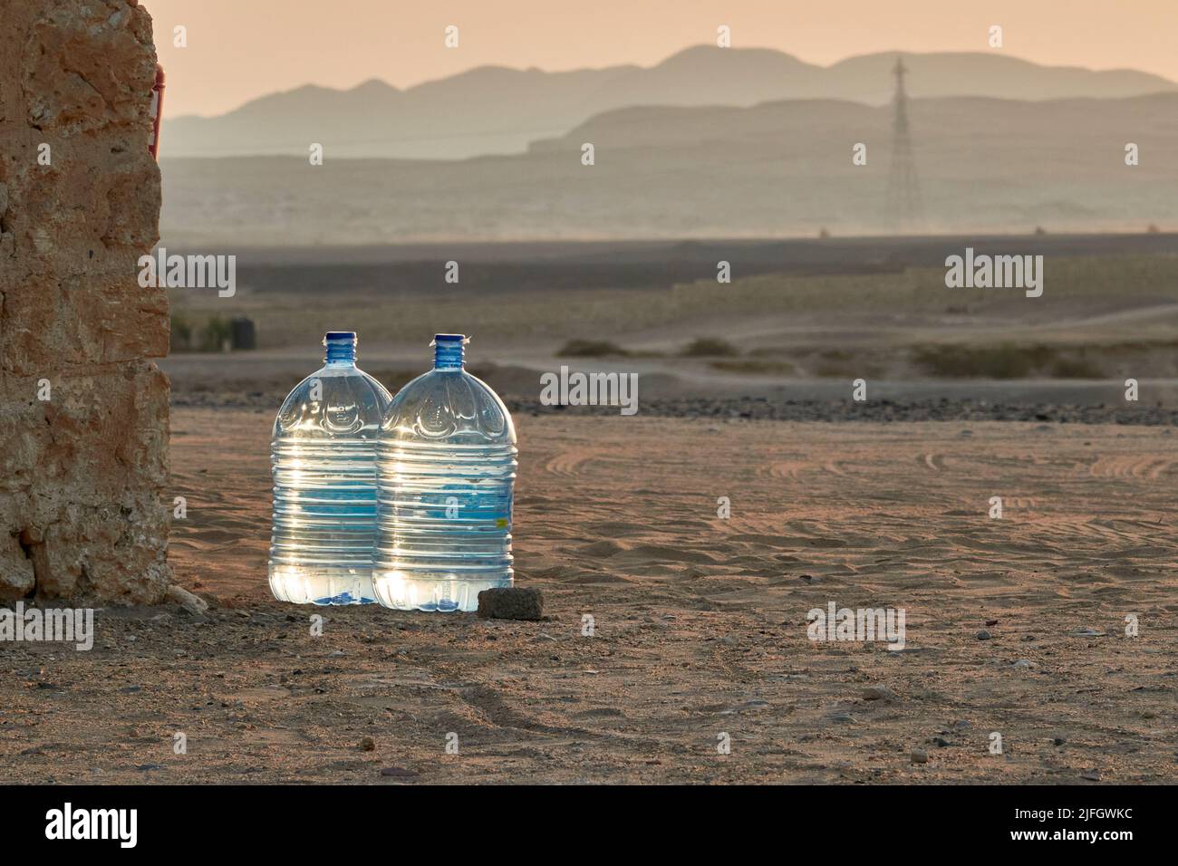 Two 2 Large Reusable Bottles With Drinking Water Stand In The Desert Sand At Sunset. Blurred Mountain Range In The Background. Marsa Alam, Egypt Stock Photo