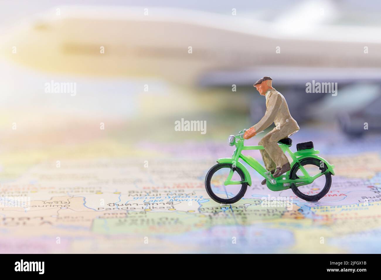 Miniature people - Figure businessman cycling on the world map with blurred white airplane background. Business finance and travel concept. Stock Photo