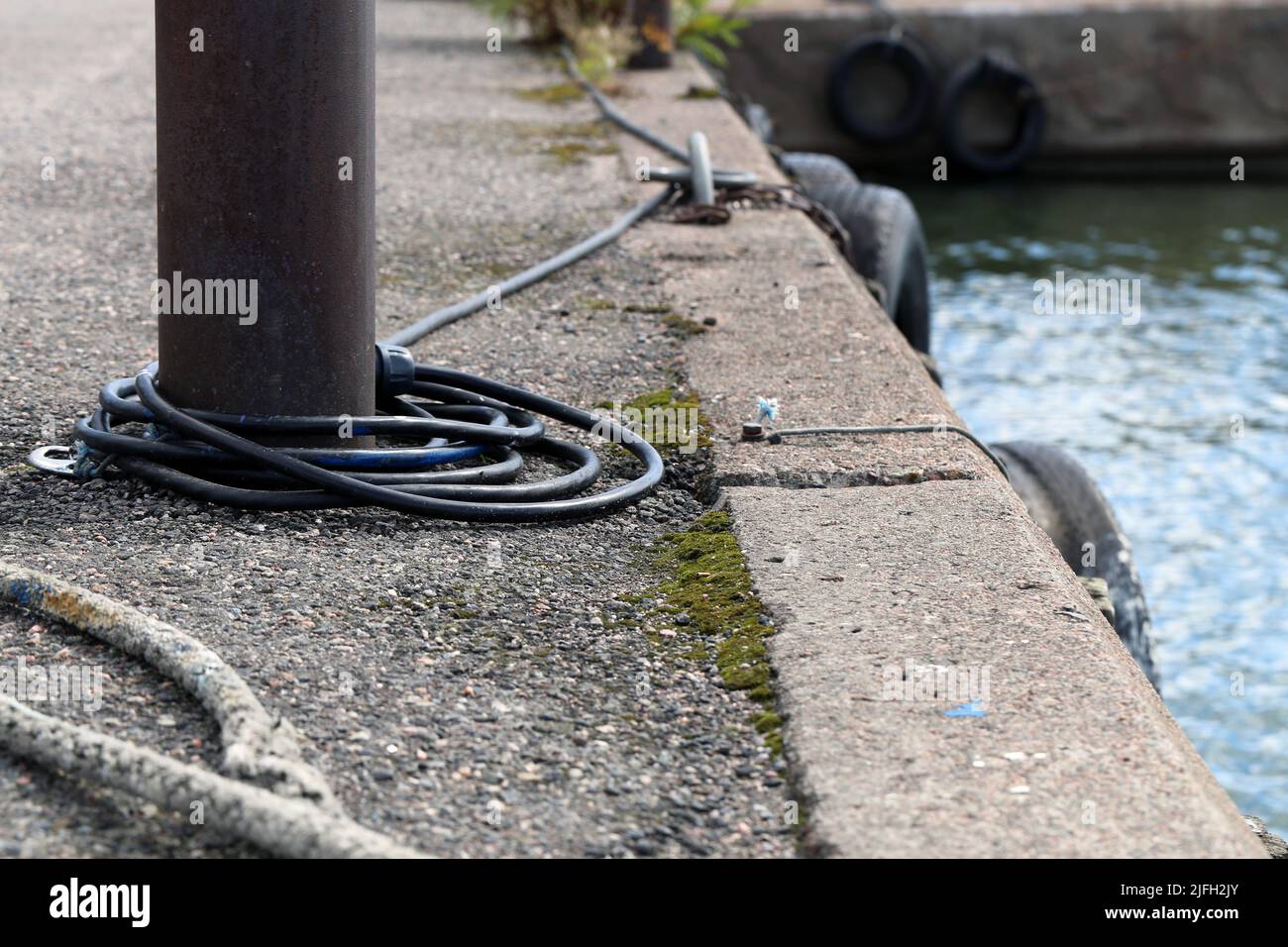 Small harbor architecture details in Helsinki, Finland, June 2019. Old rusty metal pole to which you can chain a boat. Also some concrete floor. Stock Photo