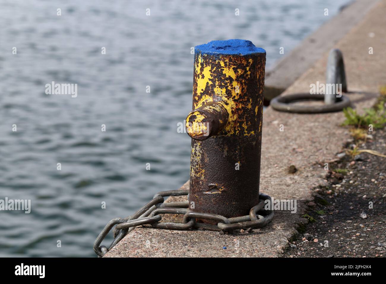 Small harbor architecture details in Helsinki, Finland, June 2019. Old rusty metal pole to which you can chain a boat. Also some concrete floor. Stock Photo
