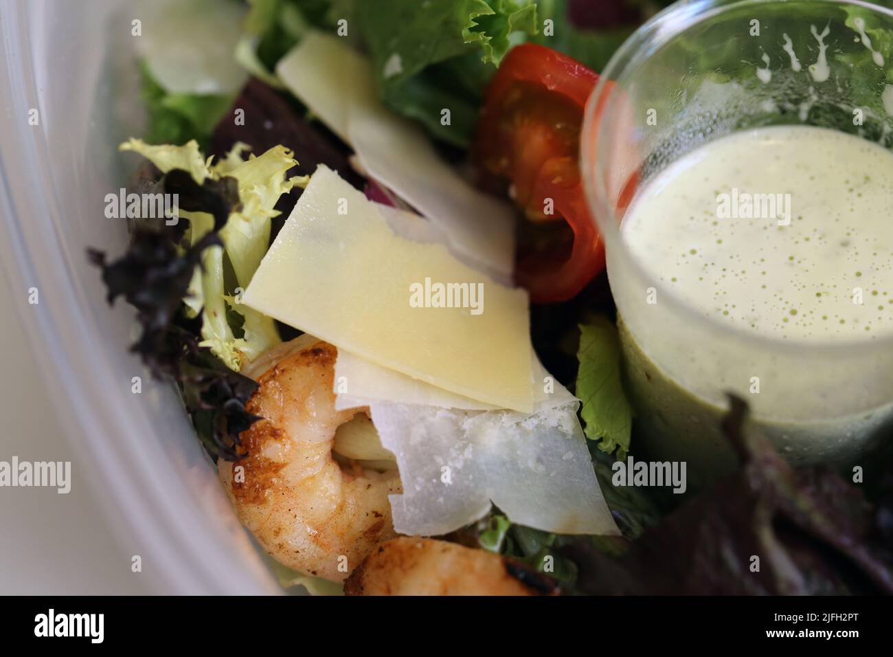 Healthy and delicious surf and turf kind of takeaway salad in a closeup. You can see some greens, chili, parmesan, scrimps, beef and salad dressing. Stock Photo