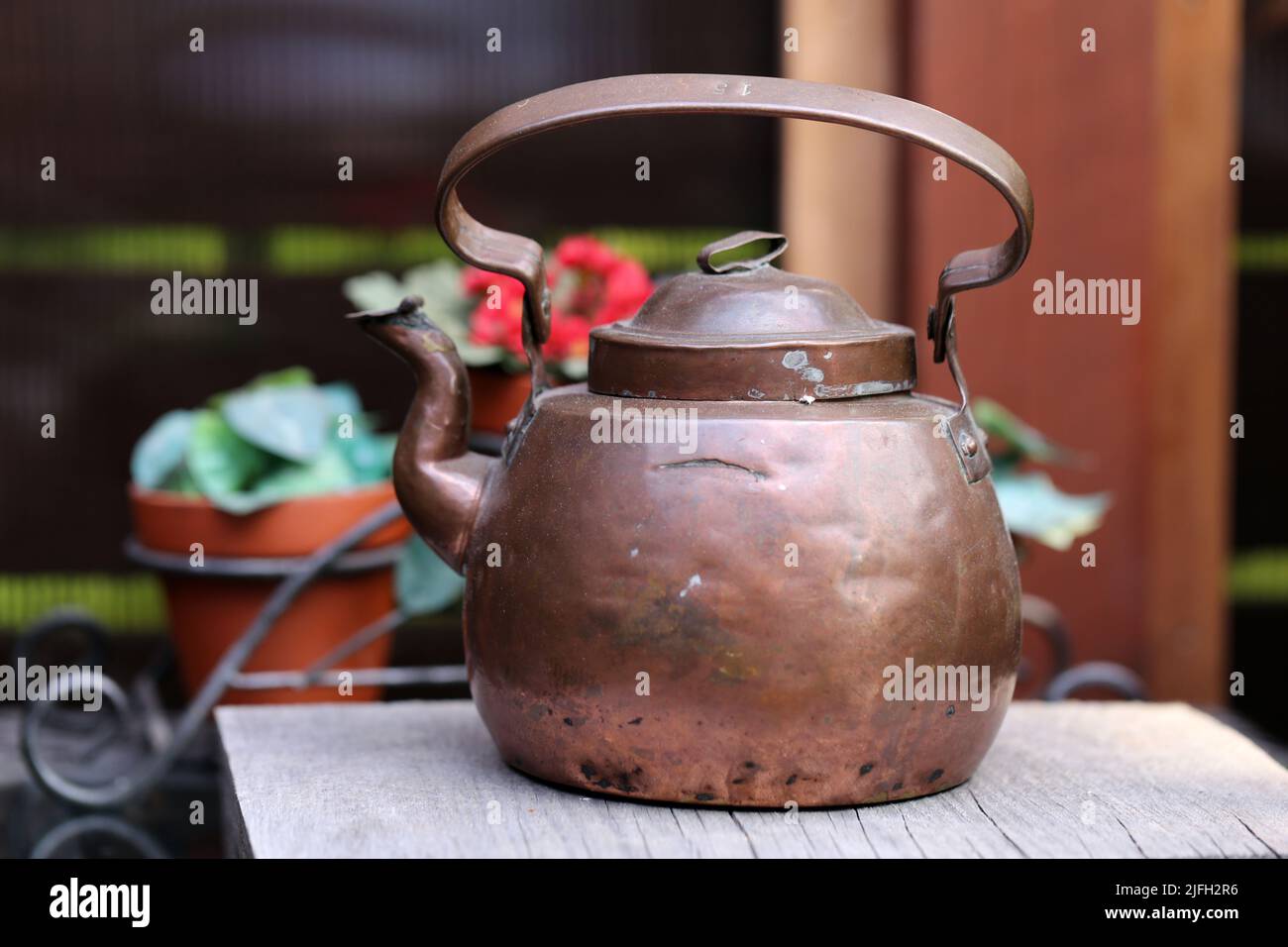 Old copper teapot photographed in a Finnish summer cottage during midsummer day. You can see some flowers and buildings in the background. Closeup. Stock Photo